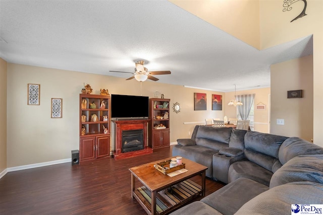 living room with a glass covered fireplace, baseboards, dark wood-type flooring, and a ceiling fan