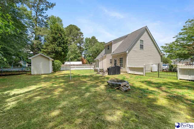 back of house with a yard, a trampoline, a storage unit, and a fenced backyard