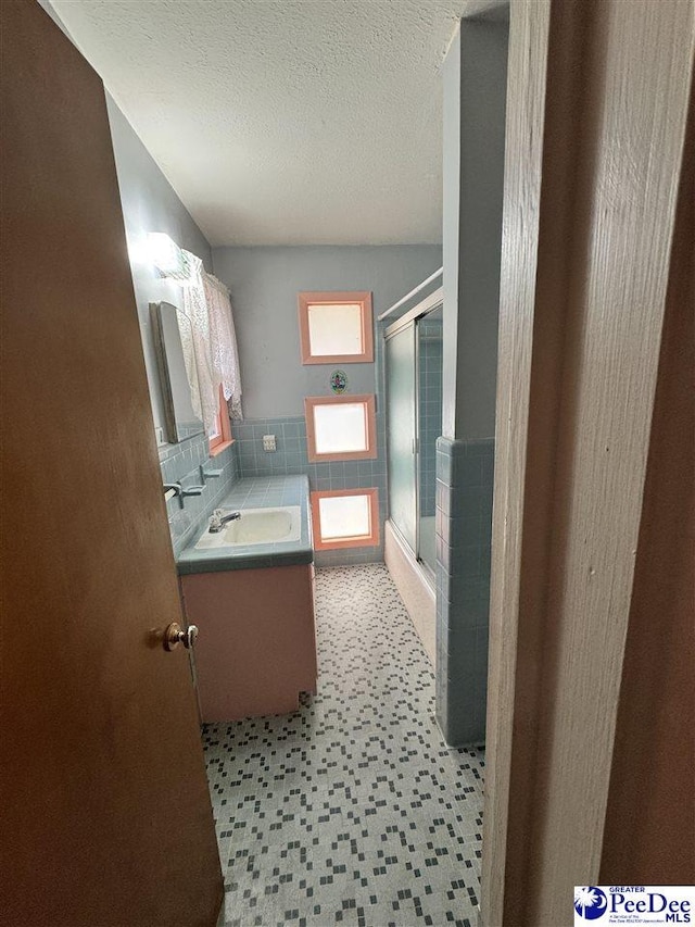 full bathroom with tile walls, a shower stall, a textured ceiling, and vanity