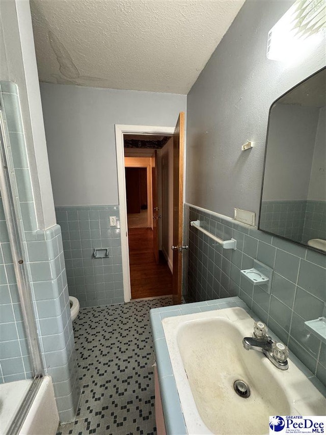 bathroom with tile walls, toilet, wainscoting, a textured ceiling, and tile patterned floors