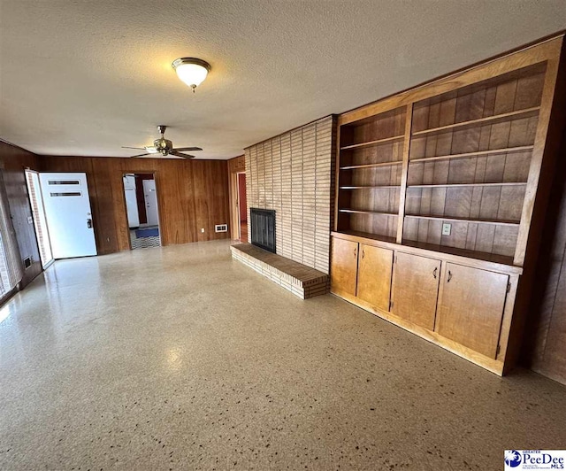 unfurnished living room featuring a fireplace, a ceiling fan, wood walls, a textured ceiling, and speckled floor