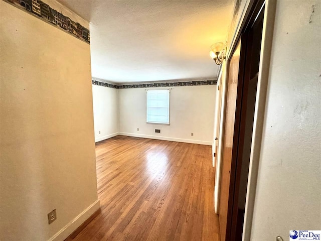 spare room with visible vents, a textured ceiling, baseboards, and wood finished floors