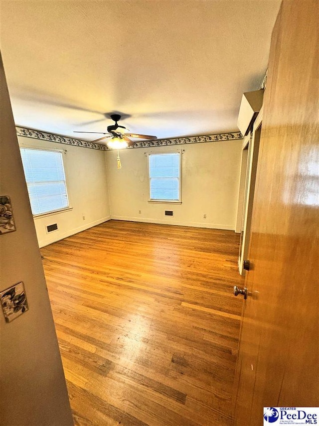 unfurnished bedroom featuring a textured ceiling, wood finished floors, a ceiling fan, visible vents, and baseboards