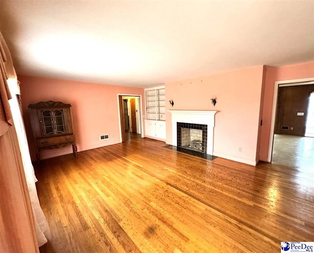 unfurnished living room featuring baseboards, visible vents, wood finished floors, and a tile fireplace