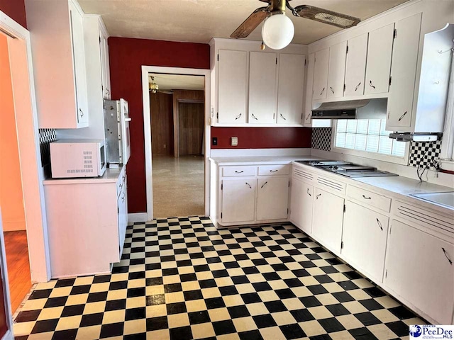 kitchen featuring dark floors, stainless steel gas cooktop, light countertops, white cabinets, and under cabinet range hood