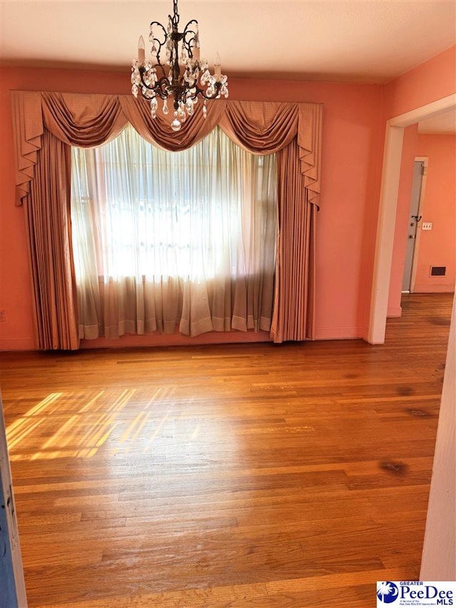 empty room with visible vents, a chandelier, and wood finished floors