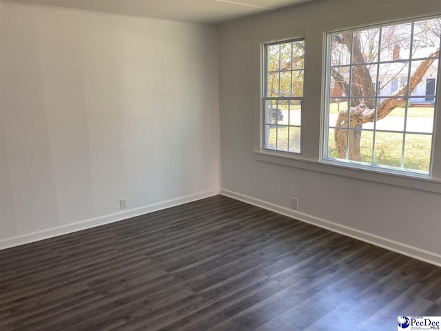 unfurnished room with dark wood finished floors, plenty of natural light, and baseboards