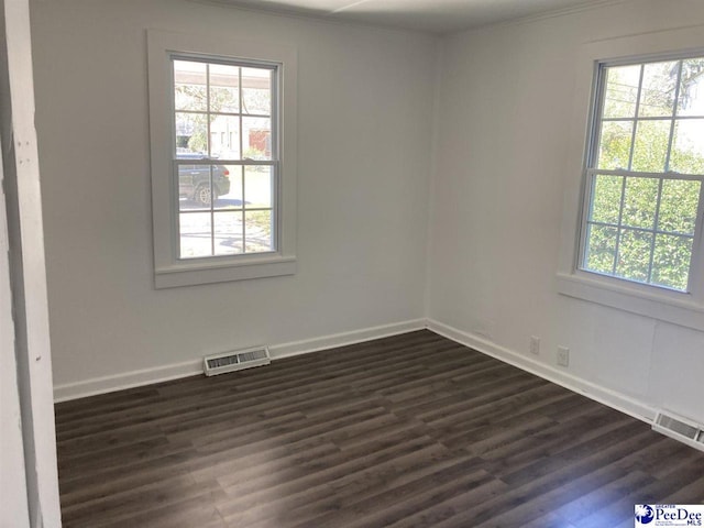 unfurnished room with a wealth of natural light, visible vents, and dark wood finished floors