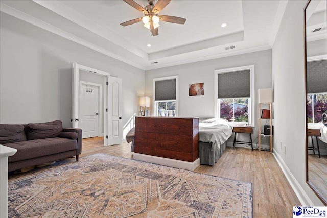 bedroom featuring light wood finished floors, visible vents, baseboards, and a tray ceiling