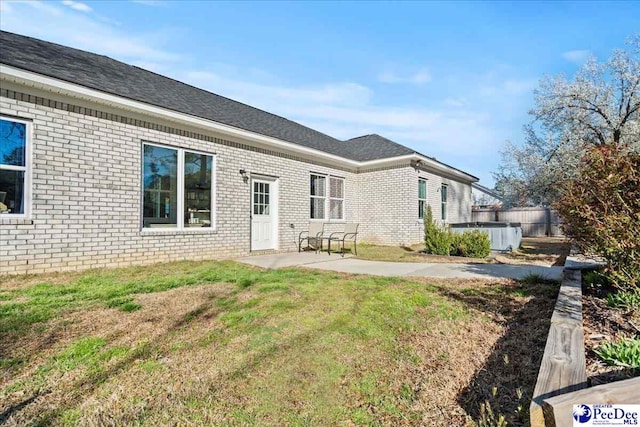 back of property with central air condition unit, a patio, a yard, brick siding, and a hot tub