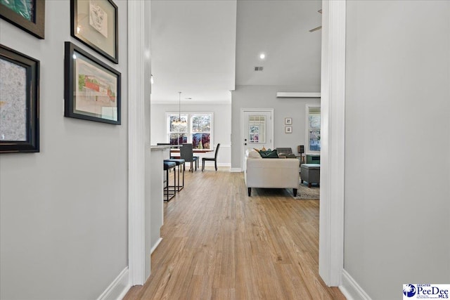 hallway featuring visible vents, light wood-type flooring, a chandelier, and baseboards