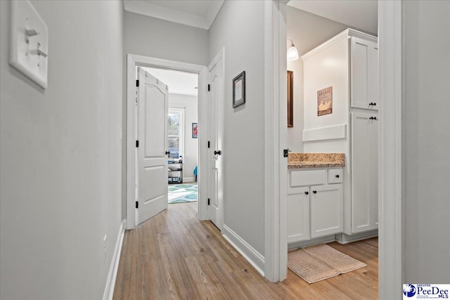 hallway with crown molding, light wood-style floors, and baseboards