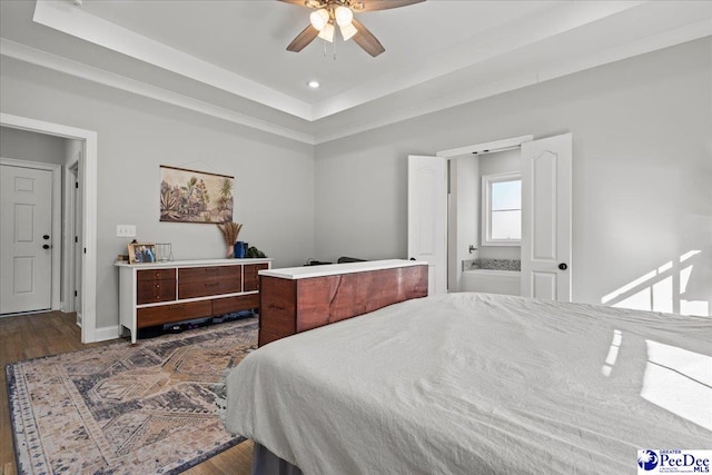 bedroom featuring ceiling fan, baseboards, a tray ceiling, wood finished floors, and ensuite bath