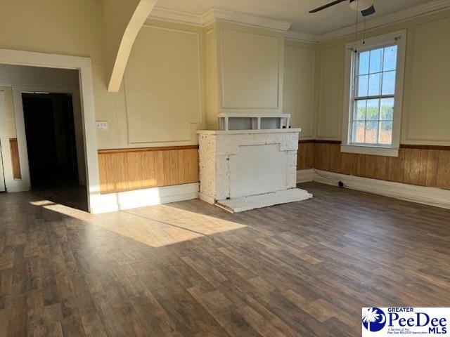 unfurnished living room featuring crown molding, ceiling fan, a fireplace, and dark wood-type flooring