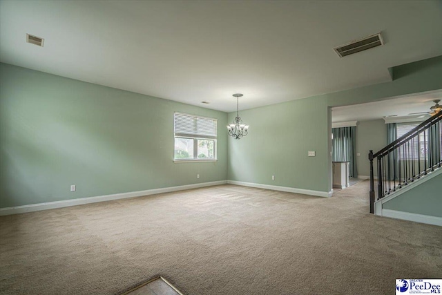 carpeted spare room featuring ceiling fan with notable chandelier