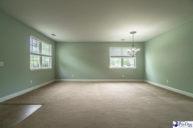 carpeted spare room featuring a healthy amount of sunlight and a chandelier