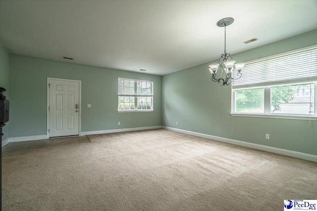 carpeted spare room featuring a healthy amount of sunlight and a notable chandelier