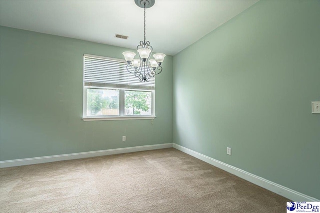 carpeted spare room featuring an inviting chandelier