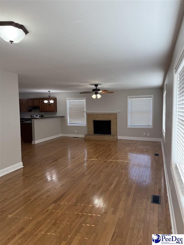 unfurnished living room featuring a brick fireplace, dark hardwood / wood-style floors, and ceiling fan with notable chandelier