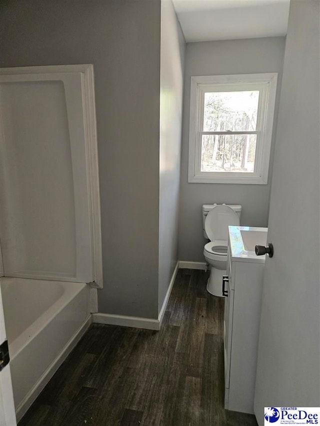 bathroom with toilet, a tub, wood finished floors, baseboards, and vanity