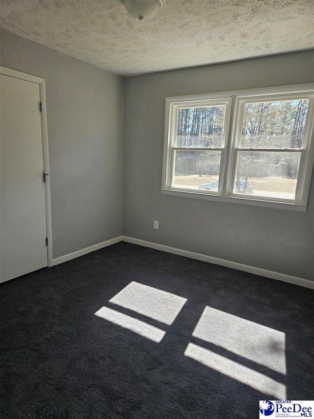 unfurnished room featuring a textured ceiling, baseboards, and dark colored carpet