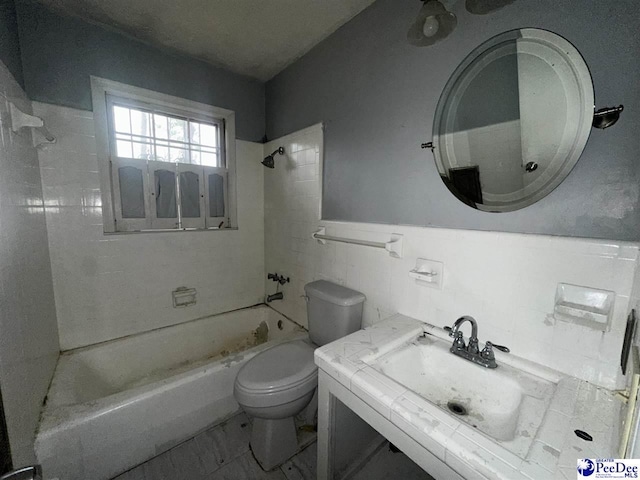 full bathroom featuring vanity, toilet, tiled shower / bath combo, and tile walls