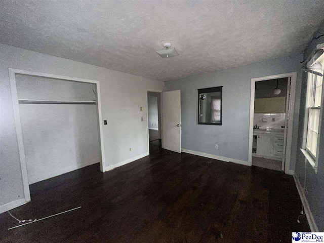 unfurnished bedroom featuring a closet, ensuite bathroom, dark hardwood / wood-style flooring, and a textured ceiling