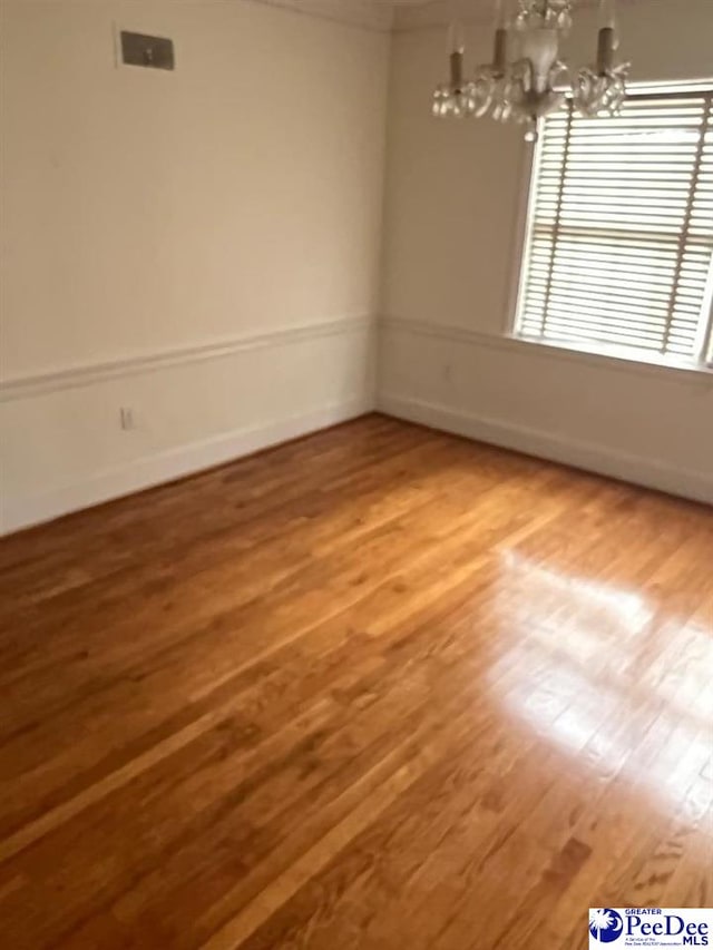 unfurnished room featuring an inviting chandelier and hardwood / wood-style floors