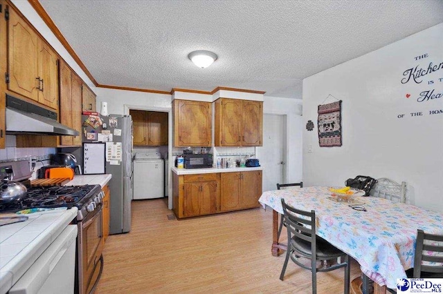 1017 Big Swamp Rd, Pamplico, SC 29583 - kitchen with stainless steel appliances, under cabinet range hood, washer / clothes dryer, tile countertops, and brown cabinets