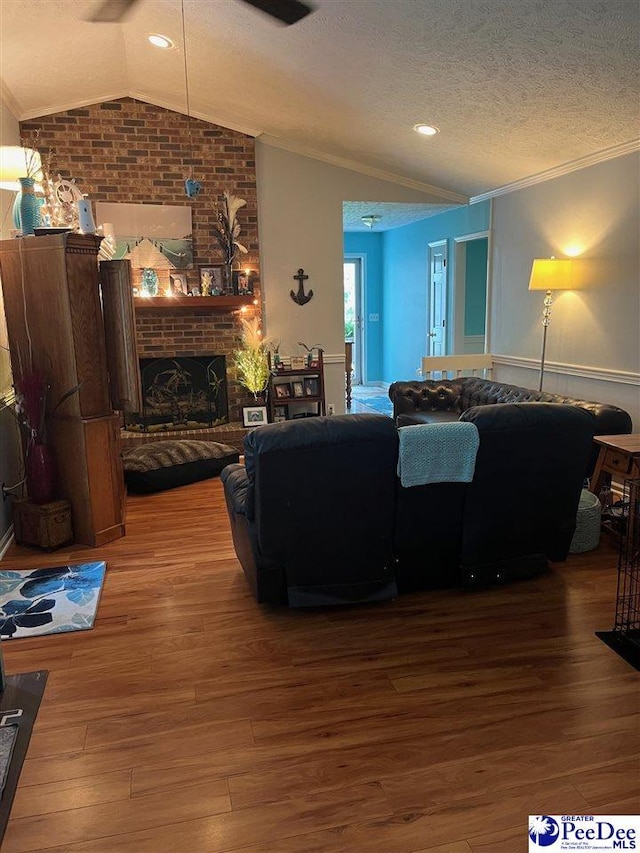 living room featuring wood-type flooring, lofted ceiling, ornamental molding, a brick fireplace, and a textured ceiling