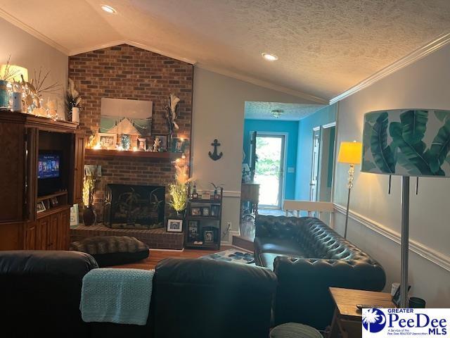 living room featuring lofted ceiling, crown molding, hardwood / wood-style flooring, a textured ceiling, and a brick fireplace