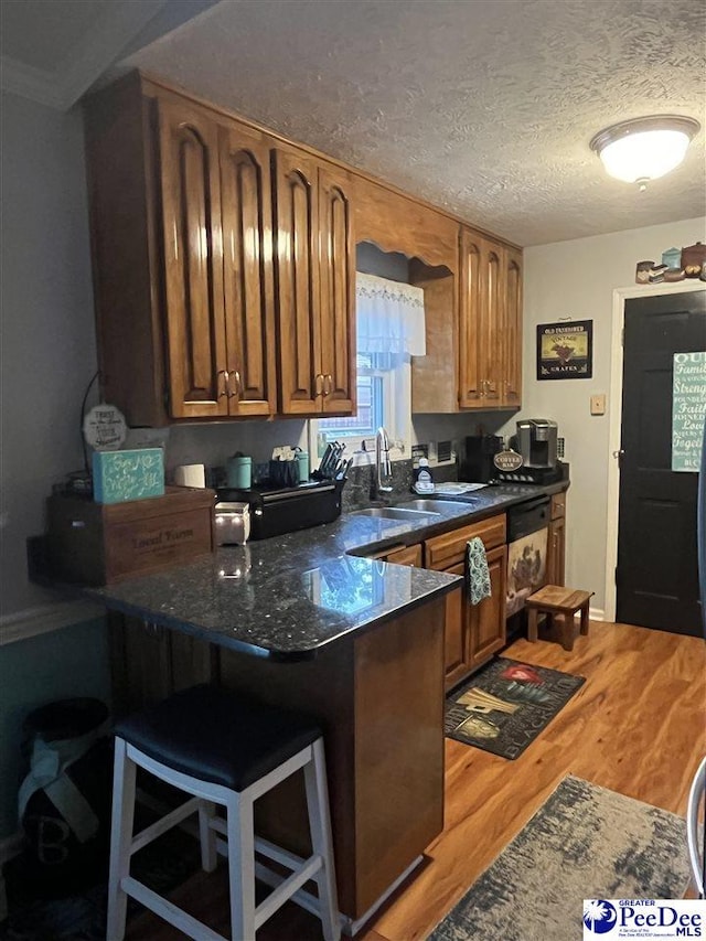 kitchen with a breakfast bar, sink, wood-type flooring, a textured ceiling, and dark stone countertops