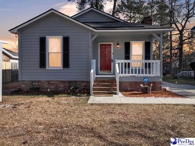 bungalow-style house with crawl space, covered porch, a shingled roof, and a chimney