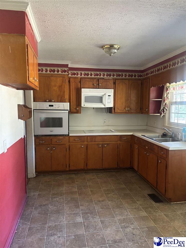 kitchen with white appliances, a sink, light countertops, brown cabinets, and crown molding