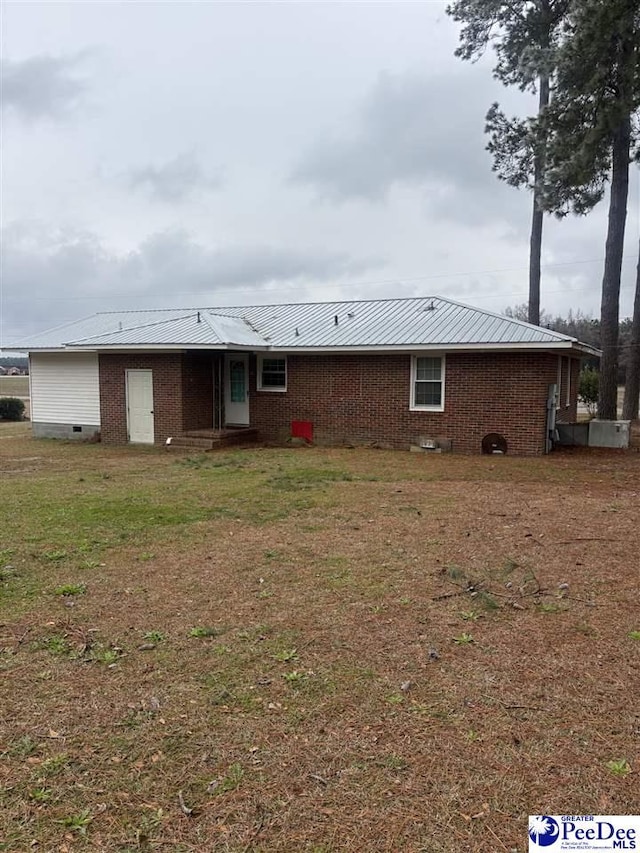 rear view of house with a yard, metal roof, and brick siding