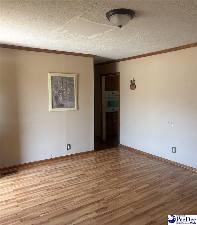 unfurnished room featuring light wood-type flooring, crown molding, a textured ceiling, and baseboards