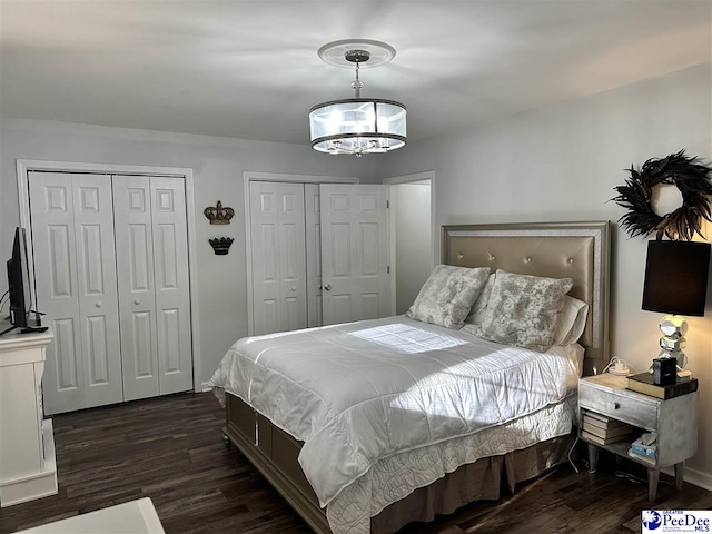bedroom featuring multiple closets, an inviting chandelier, and dark wood-type flooring