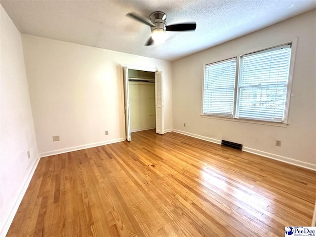 unfurnished bedroom with ceiling fan, light hardwood / wood-style flooring, a closet, and a textured ceiling