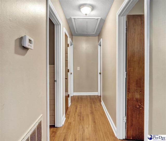 hallway with a textured ceiling and light hardwood / wood-style flooring