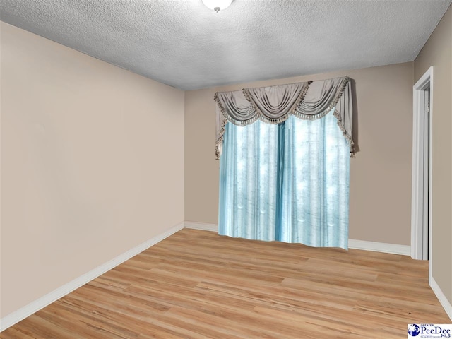 empty room with a textured ceiling and light hardwood / wood-style flooring