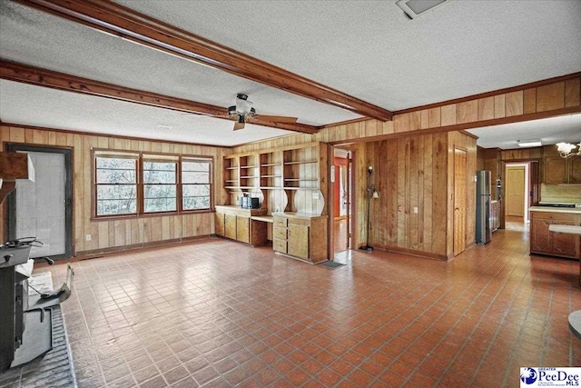 unfurnished living room with ornamental molding, beam ceiling, wooden walls, and a textured ceiling