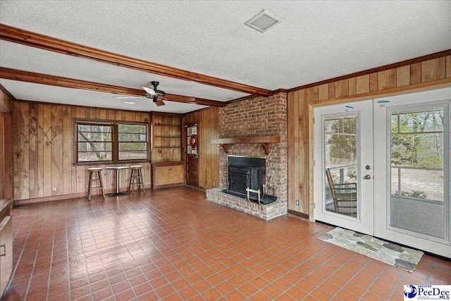 unfurnished living room with french doors, visible vents, wooden walls, a textured ceiling, and beamed ceiling