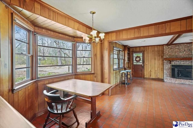 dining area with wooden walls, breakfast area, beamed ceiling, an inviting chandelier, and a fireplace