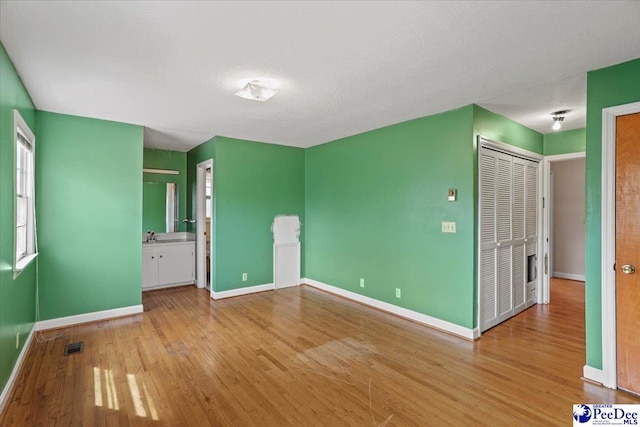 unfurnished bedroom with ensuite bath, visible vents, baseboards, and wood finished floors