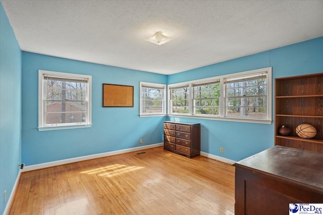 unfurnished office with baseboards, a textured ceiling, and hardwood / wood-style floors