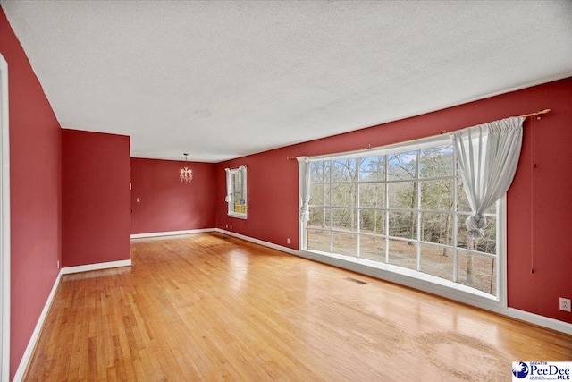 unfurnished living room featuring visible vents, a textured ceiling, wood finished floors, a chandelier, and baseboards