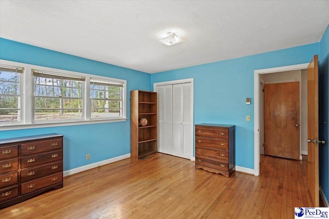 bedroom with a closet, a textured ceiling, baseboards, and wood finished floors