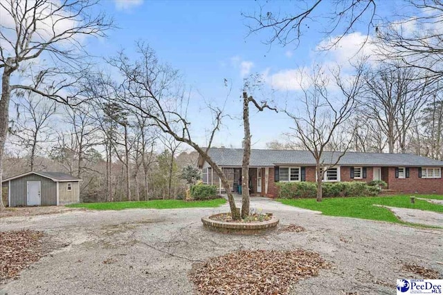 ranch-style house with an outbuilding, brick siding, curved driveway, a storage shed, and a front yard