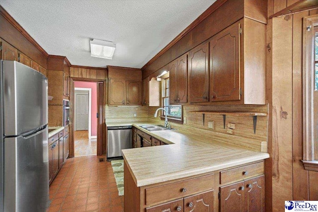 kitchen with stainless steel appliances, light countertops, backsplash, ornamental molding, and a sink