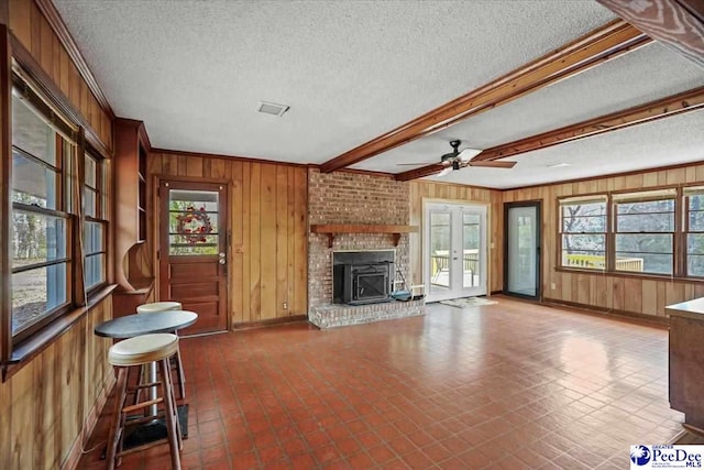 unfurnished living room with beam ceiling, a ceiling fan, wood walls, a textured ceiling, and baseboards